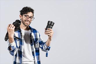 Portrait of smiling photographer man showing a camera and lens on isolated background. Smiling young man holding a camera isolated