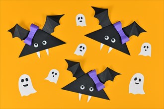 Origami paper vampire bats with googly eyes and ghosts and spiders on yellow Halloween background
