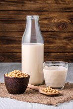 Bottle of soy milk with soybeans on white table over dark wooden background