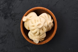 Top view of uncooked khinkali in wooden plate on black wooden background
