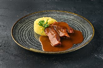 Roasted beef slices with wine sauce and mashed potato on dark background