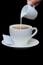 Pouring milk in coffee. Photo with clipping path isolated on black background
