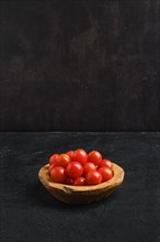 Fresh tomato cherry in wooden bowl on dark background