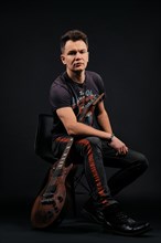 Low key portrait of musician sitting on chair with electro guitar