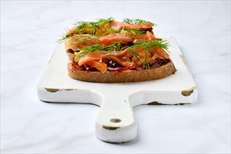Serving board with salmon sandwich with caramelized onion on wooden serving board