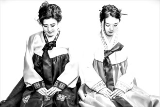 Two seated woman in Korean traditional costume bowing their heads