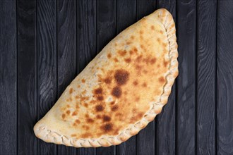 Fresh baked pizza calzone on dark wooden table