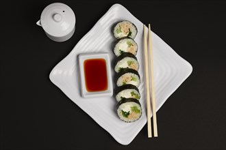 Top view of portion of chicken teriyaki rolls served on black paper with soy sauce and hashi