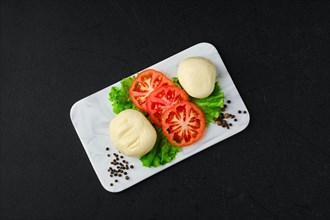 Overhead view of mozzarella with slices of fresh tomato on marble serving plate