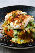 Closeup view of poached egg on a bun with avocado on a plate