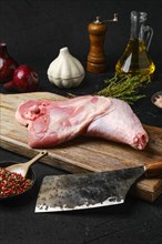 Raw turkey leg with skin on cutting board with cooking ingredients on black background