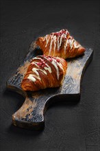 Two crispy croissant with raspberry on rustic wooden serving board