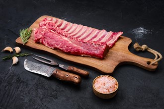 Fresh raw rack of lamb on wooden cutting board with herbs and seasoning