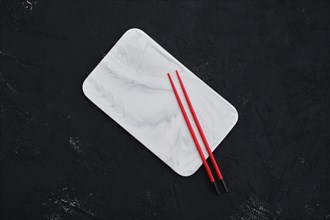 Overhead view of empty marble platter and hashi on dark background
