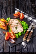 Sliced baked ham with fresh tomatoes on a stone plate in a rustic style