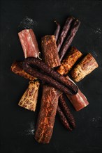 Assortment of dry-cured beef meat and sausages on dark background