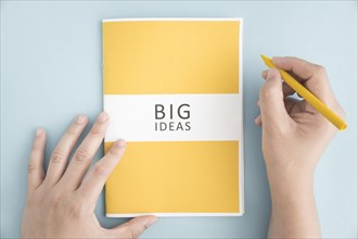 Close up person holding yellow crayon with big idea book blue background