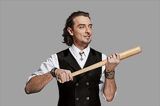 Dramatic man in white shirt and black vest with long curly hair holding baseball bat