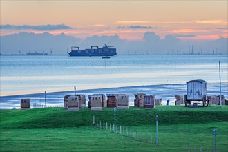 Grassy beach with beach chairs and container ship on the Weser at dusk