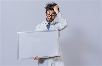 Male scientist in white coat holding and pointing at a blank whiteboard. Disheveled-haired man holding blank whiteboard