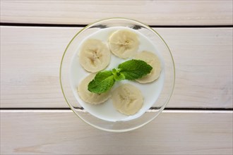 Top view of glass with yogurt and raw honey topped with sliced bananas and mint leaf. Selective focus photo