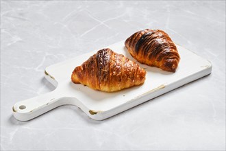 Crispy croissant on wooden serving board on marble background