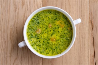 Top view of green soup with asparagus and small sausage on wooden table