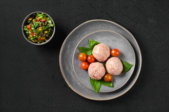 Top view of semifinished frozen veal meatballs on a plate with basil and tomato