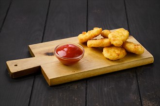 Crispy chicken nuggets in breading served with ketchup on wooden board