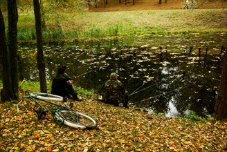 Three men fishing in the pond in autumn time