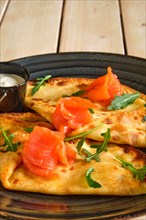 Close up view of thin pancakes with salmon and sour cream