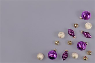 Christmas flat lay with purple and white tree ornament baubles and golden bells in corner of gray background with empty copy space