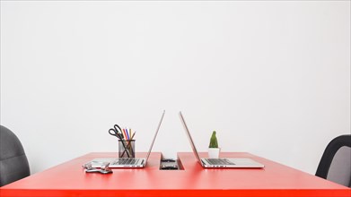 Modern workplace with two laptops red table against white wall