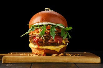 Burger with double beef cutlet and bacon on wooden serving board over black background