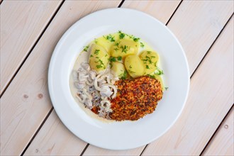 Top view of fried chicken fillet in rosemary breading served with boiled potato and mushroom creamy sauce