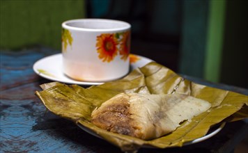 Traditional Tamal Pisque stuffed with a cup of coffee served on the table. Tamal Pisque stuffed typical Nicaraguan food. View of a stuffed tamale with a cup of coffee served on a wooden table