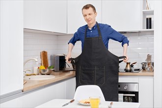 Mid adult man takes off his apron before eating the breakfast he has prepared by himself