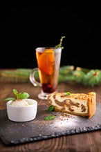 Layered cheesecake with ice cream and fruit tea served on slate plate on dark wooden background