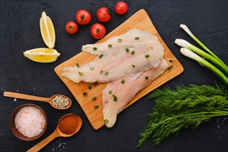 Top view of raw fresh haddock fillet on wooden cutting board with spice and herbs