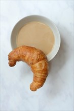 Coffee with milk in bowl and croissant