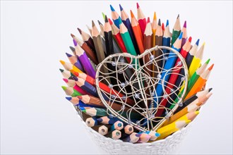 Color Pencils and heart shaped metal wire cage on a white background