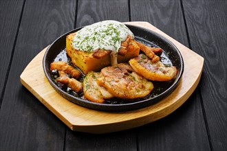 Potato casserole with fried pork mini belly slices on dark wooden table