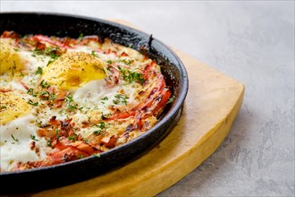 Closeup view of eggs with bell pepper and tomato baked in oven in cast-iron skillet