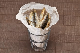 Fried sprat in rough facetted glass in wrapping paper on wooden table