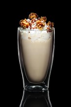Double walled glass with coffee cocktail decorated with whipped cream and popcorn isolated on black