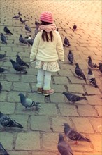 Little girl amid grey pigeons live in large groups in urban environment