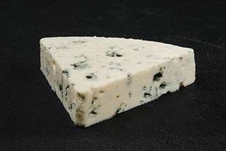 Macro photo of piece of cheese with blue mold on black background