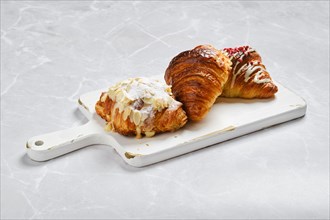 Assortment of fresh croissants on white serving board on marble background