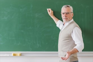 Senior male professor explaining writing green chalkboard