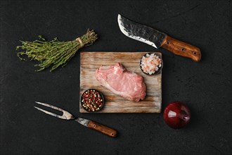 Overhead view of raw veal steak bone in with ingredients for cooking on black background